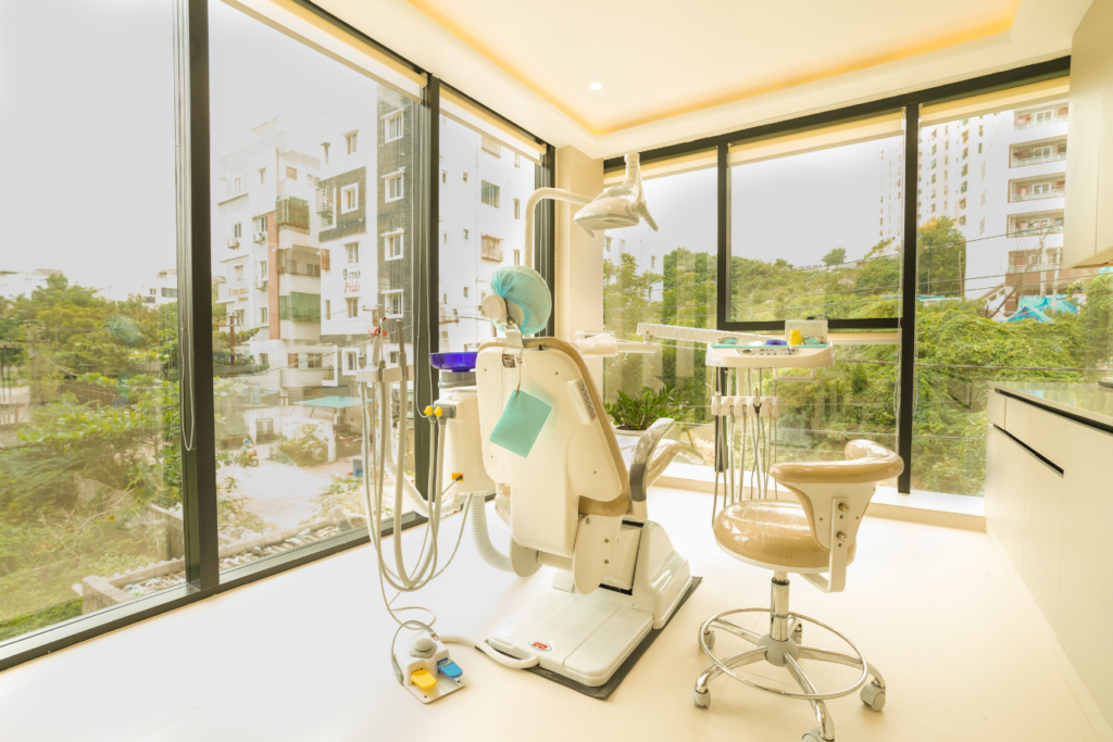 Bright, modern dental treatment room featuring a white dental chair, overhead light, and various instruments on a tray by large windows overlooking a cityscape.