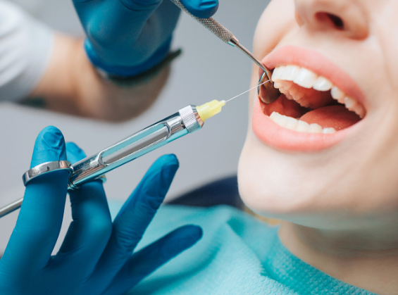 Dentist in blue gloves using a dental drill and mirror on a patient’s open mouth during a dental procedure.